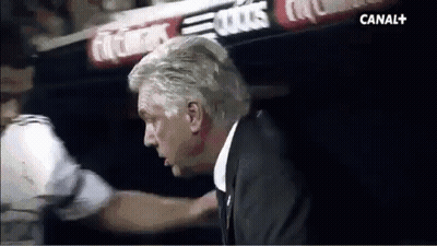 A Man In A Suit Is Talking To A Man In A White Shirt In A Dark Room . GIF