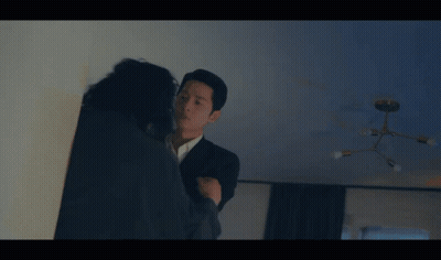 A Man In A Suit Is Talking To A Woman In A Dark Room GIF
