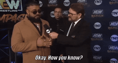 A Man In A Suit Is Talking To Another Man In Front Of A Wall That Says Aew GIF
