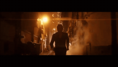 A Man In A Suit Is Walking Down A Dark Alley At Night GIF
