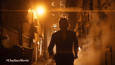 A Man In A Suit Is Walking Down A Dark Alleyway With The Hashtag #Clayfacemovie Below Him GIF
