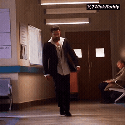 A Man In A Suit Is Walking Down A Hallway With A Sign That Says X7wick Reddy On It GIF