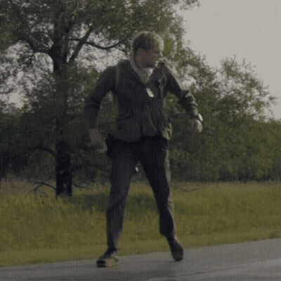 A Man In A Suit Is Walking Down A Street GIF