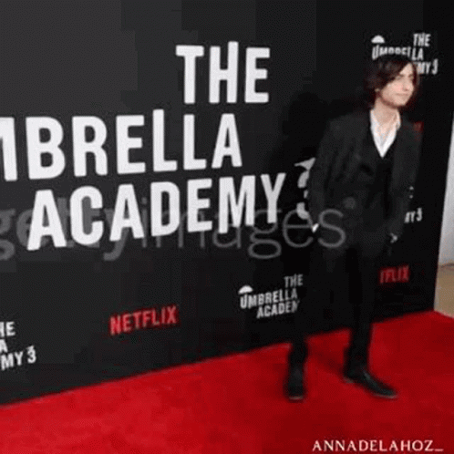 A Man In A Suit Is Walking On A Red Carpet At The Umbrella Academy Premiere . GIF