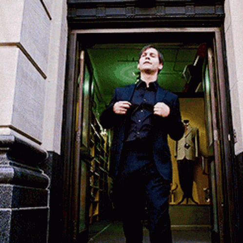 A Man In A Suit Is Walking Out Of A Doorway GIF