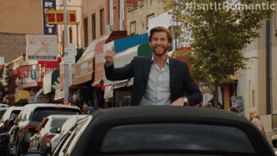A Man In A Suit Is Waving From The Back Of A Car In A City GIF