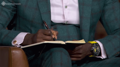 A Man In A Suit Is Writing In A Notebook With #Cbcdragonsden Written On The Bottom GIF