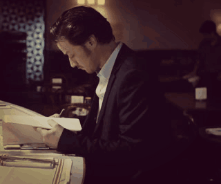 A Man In A Suit Is Writing On A Piece Of Paper In A Dark Room GIF
