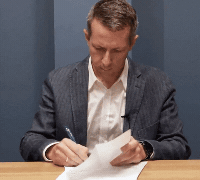 A Man In A Suit Is Writing On A Piece Of Paper With A Pen GIF