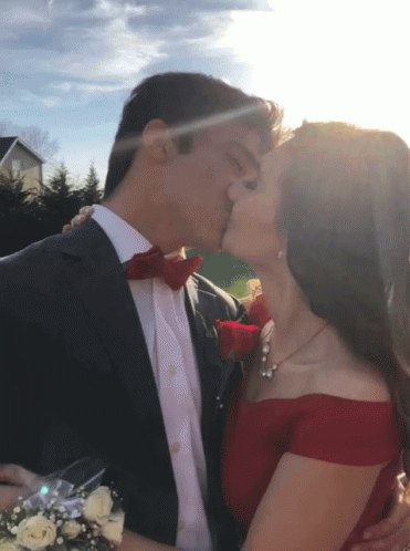 A Man In A Suit Kisses A Woman In A Red Off The Shoulder Dress GIF