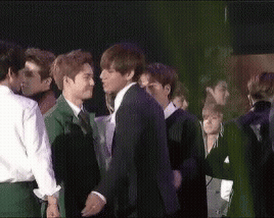 A Man In A Suit Kisses Another Man In A Crowd Of People GIF