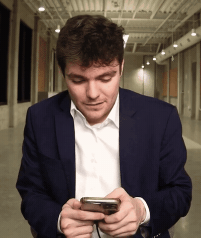 A Man In A Suit Looks At His Cell Phone GIF