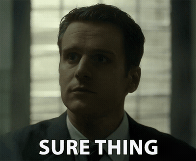 A Man In A Suit Says Sure Thing In Front Of Him GIF