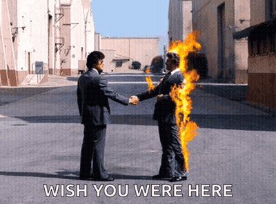 A Man In A Suit Shakes Hands With A Man In A Burning Suit With The Words Wish You Were Here Below Them GIF