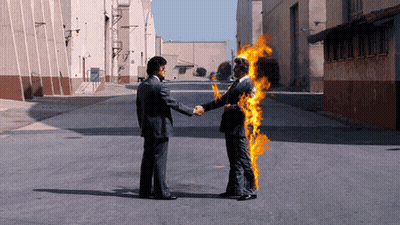 A Man In A Suit Shakes Hands With A Man In A Fire Suit GIF