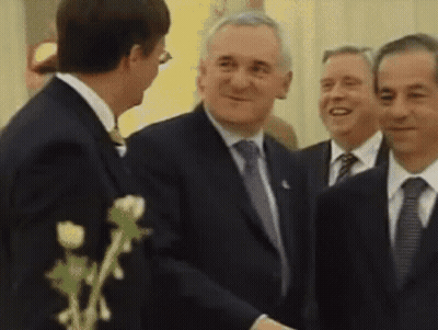 A Man In A Suit Shakes Hands With Another Man In A Suit And Tie GIF