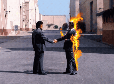 A Man In A Suit Shakes Hands With Another Man In A Suit That Is On Fire GIF