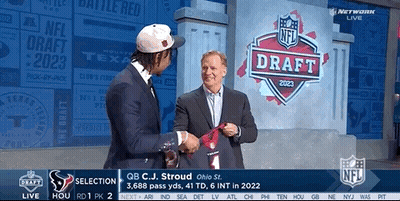 A Man In A Suit Shakes Hands With Another Man In Front Of A Nfl Draft Sign GIF