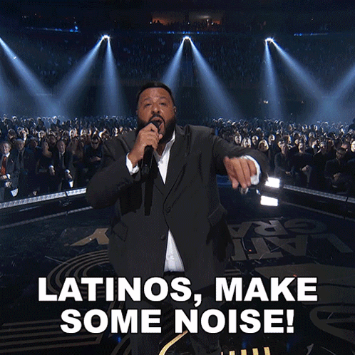 A Man In A Suit Singing Into A Microphone With The Words Latinos Make Some Noise Below Him GIF