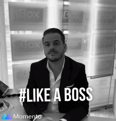 A Man In A Suit Sits At A Desk In Front Of A Window That Says Box On It GIF