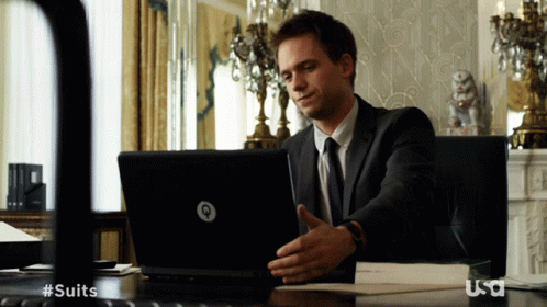 A Man In A Suit Sits At A Desk With A Laptop And A Usa Logo GIF