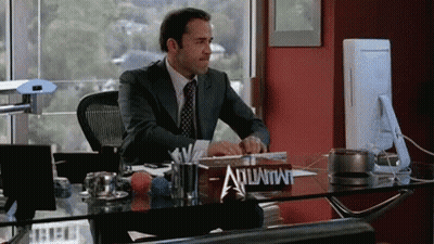A Man In A Suit Sits At A Desk With A Sign That Says Advantage On It GIF