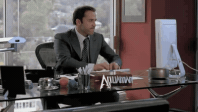 A Man In A Suit Sits At A Desk With A Sign That Says Atlantis On It GIF