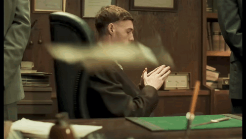 A Man In A Suit Sits At A Desk With His Hands Folded In Front Of Him GIF