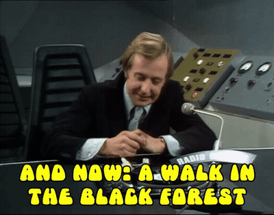 A Man In A Suit Sits At A Desk With The Words And Now A Walk In The Black Forest Above Him GIF