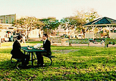 A Man In A Suit Sits At A Picnic Table In A Park GIF