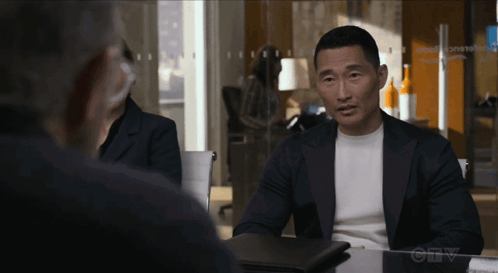 A Man In A Suit Sits At A Table In Front Of A Sign That Says " Ctv " On It GIF