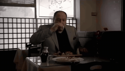 A Man In A Suit Sits At A Table With A Plate Of Food And A Glass Of Wine GIF