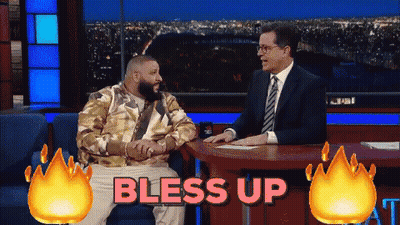 A Man In A Suit Sits At A Table With The Words Bless Up Behind Him GIF