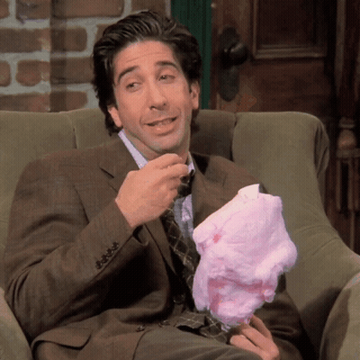 A Man In A Suit Sits In A Chair Eating Cotton Candy GIF