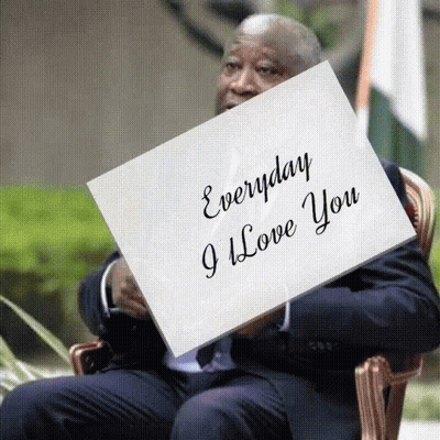 A Man In A Suit Sits In A Chair Holding A Piece Of Paper That Says Everyday I Love You GIF