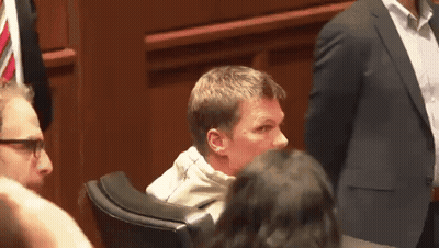 A Man In A Suit Sits In A Chair With A Woman Behind Him GIF