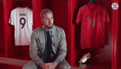 A Man In A Suit Sits In A Locker With Kane Jerseys GIF