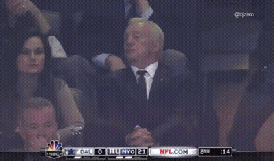 A Man In A Suit Sits In A Stadium Watching A Game Between Dallas And New York Giants GIF