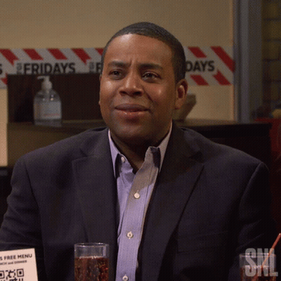 A Man In A Suit Sits In Front Of A Sign That Says Fridays On It GIF