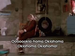 A Man In A Suit Sits On A Stone Ledge With Oklahoma Oklahoma Written On The Bottom GIF