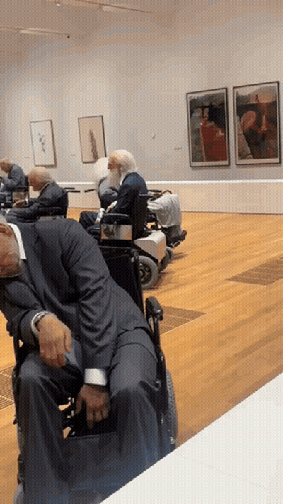 A Man In A Suit Sleeping In A Wheelchair In A Museum GIF