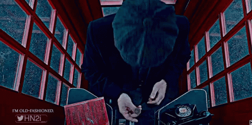 A Man In A Suit Smoking A Cigar In A Red Phone Booth GIF