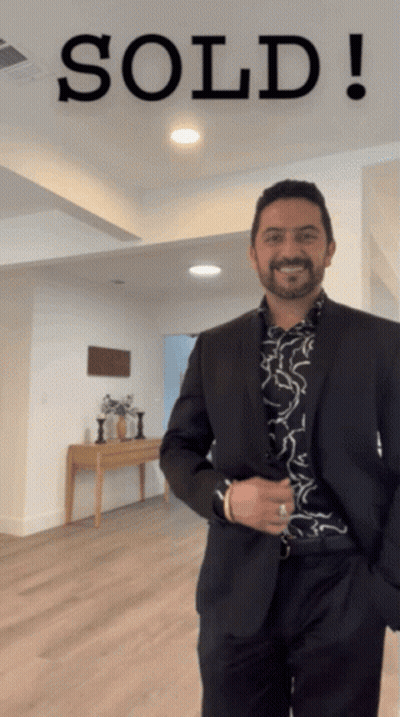 A Man In A Suit Standing In Front Of A Sold Sign GIF