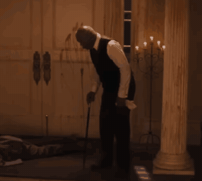 A Man In A Suit Stands In A Dark Room GIF