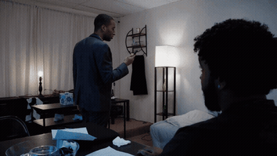 A Man In A Suit Stands In A Dark Room Talking To Another Man GIF