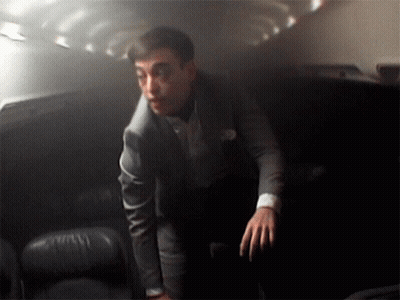 A Man In A Suit Stands In A Dark Room With His Hands On His Hips GIF