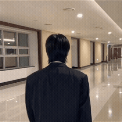 A Man In A Suit Stands In A Hallway With His Back To The Camera GIF