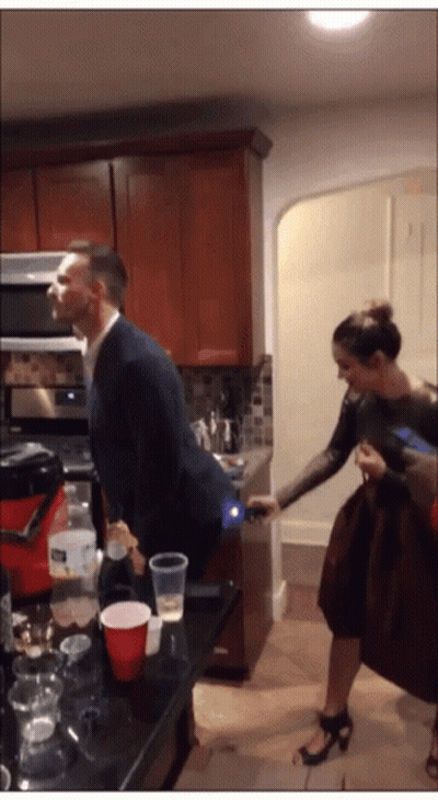 A Man In A Suit Stands In A Kitchen With A Woman Standing Behind Him GIF