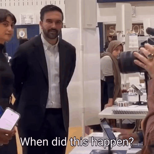 A Man In A Suit Stands In Front Of A Camera With The Words When Did This Happen Behind Him GIF