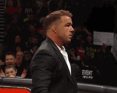 A Man In A Suit Stands In Front Of A Crowd With A Sign That Says Tna On It GIF